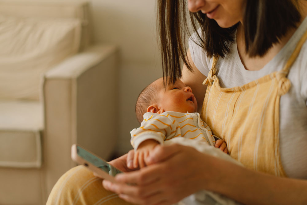 madre sosteniendo a su bebé mientras utiliza el móvil