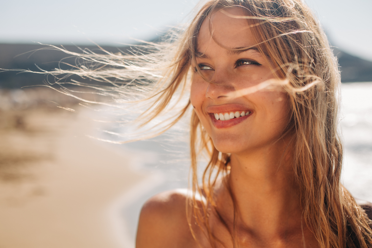 mujer sonriendo con la playa de fondo