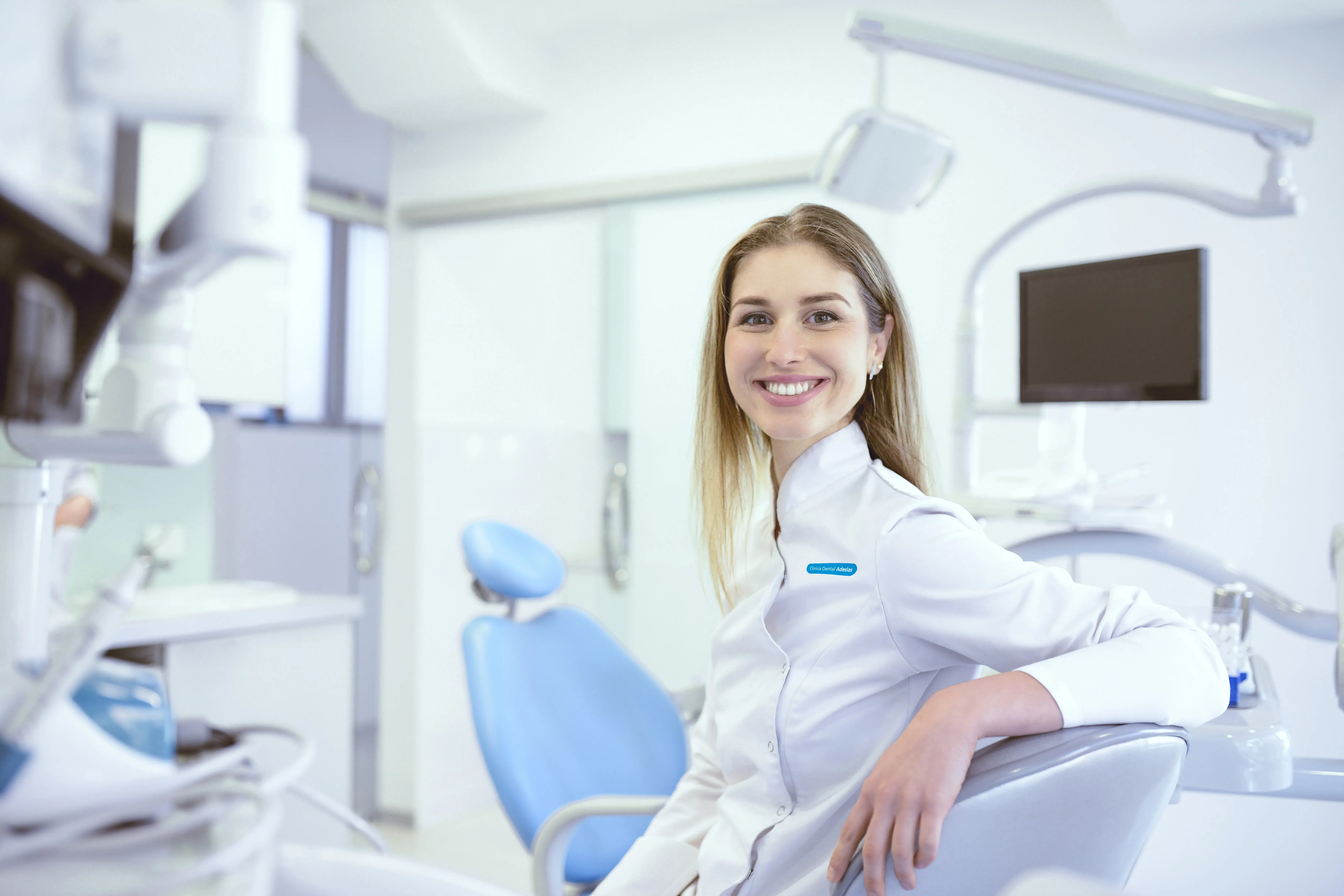 Mujer dentista mirando al frente sonriendo. Detrás el gabinete médico con los utensilios.