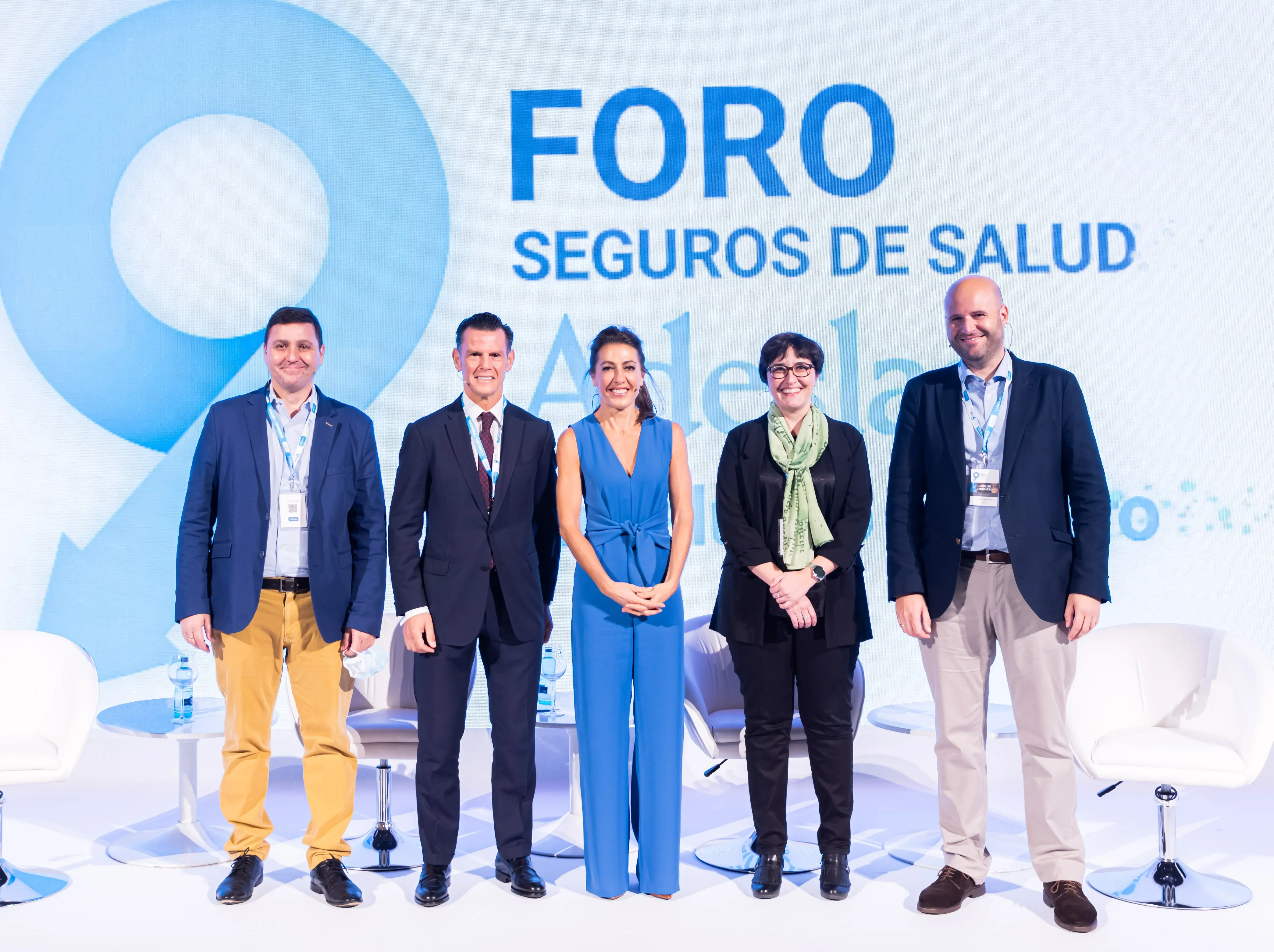 Dos mujeres y tres hombres de pie delante de unas sillas en un foro de seguros de salud